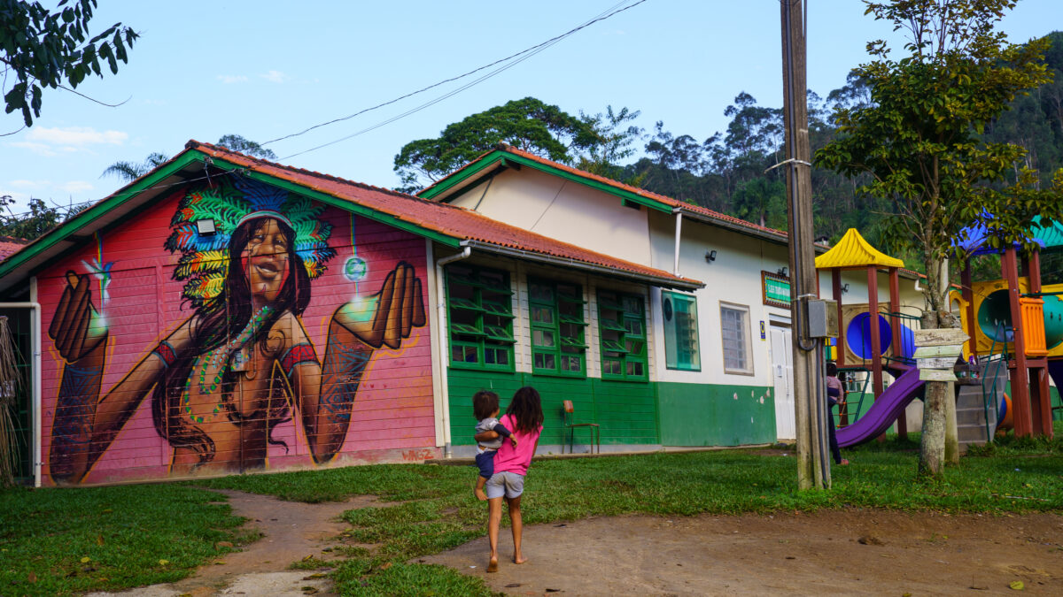 Escola da Aldeia Tekoá Marangatu com mural de mulher indígena Guarani e crianças caminhando no pátio