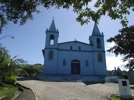 Igreja colonial azul e branca da comunidade de Sítio Novo, em Imaruí, Santa Catarina, com duas torres sineiras, portas azuis e céu limpo, marco da comunidade a 800 metros do PIER8 na SC-437